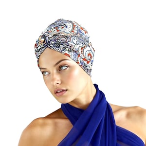 May include: A patterned turban with a paisley design in shades of blue, red, and white. The turban is worn with a draped blue fabric. The image is set against a white background.