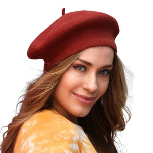 May include: A woman wearing a red beret and a yellow and white tie-dye shirt.