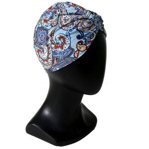 May include: A light blue turban with a paisley pattern in red, white, and blue. The turban is displayed on a black mannequin head, showcasing the head covering's design and fit. The fabric appears soft and lightweight.