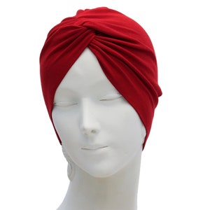 May include: A deep red turban-style head covering. The fabric is gathered and twisted at the front, creating a stylish and comfortable accessory. The head covering is displayed on a white mannequin head.