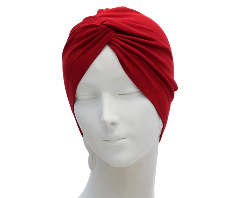 May include: A deep red turban-style head covering. The fabric is gathered and twisted at the front, creating a stylish and comfortable accessory. The head covering is displayed on a white mannequin head.