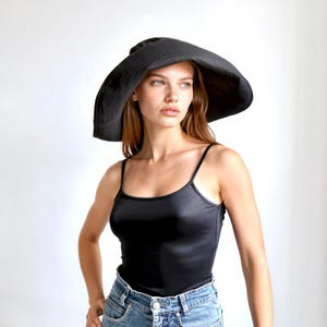 May include: A black sun hat with a wide brim. The hat is made of a soft material and is worn by a person wearing a black tank top and blue jeans.