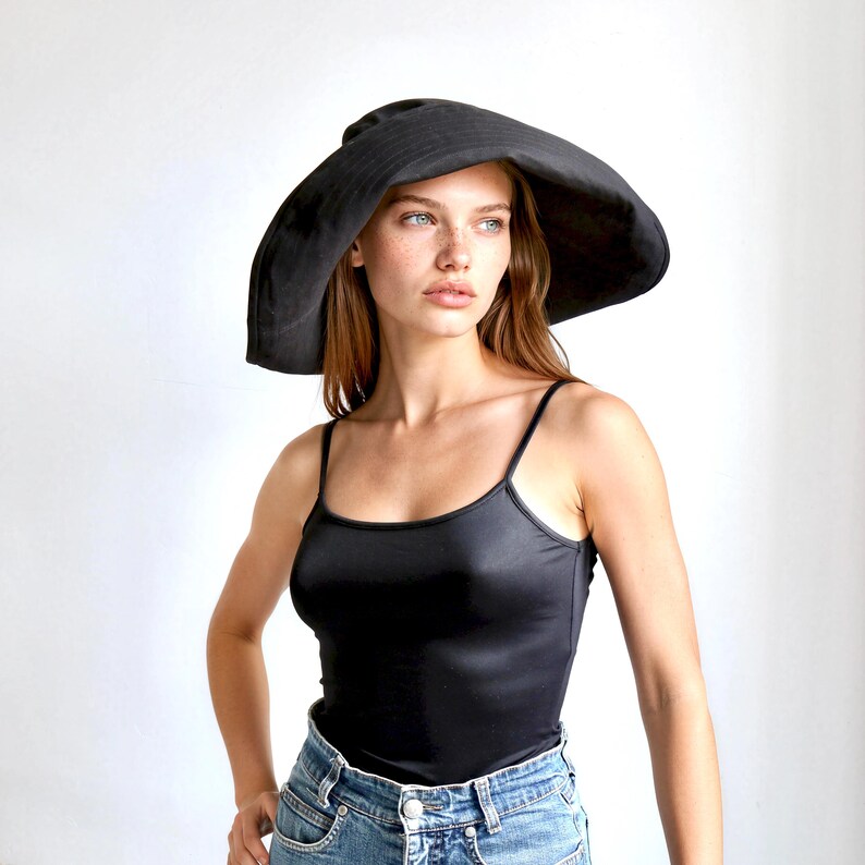 May include: A black sun hat with a wide brim. The hat is made of a soft material and is worn by a person wearing a black tank top and blue jeans.