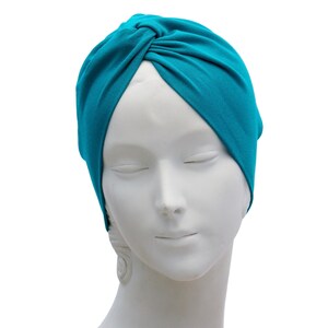 May include: A teal-colored turban-style head covering. The fabric is gathered and knotted at the top, creating a stylish and comfortable accessory. The head covering is displayed on a white mannequin head.