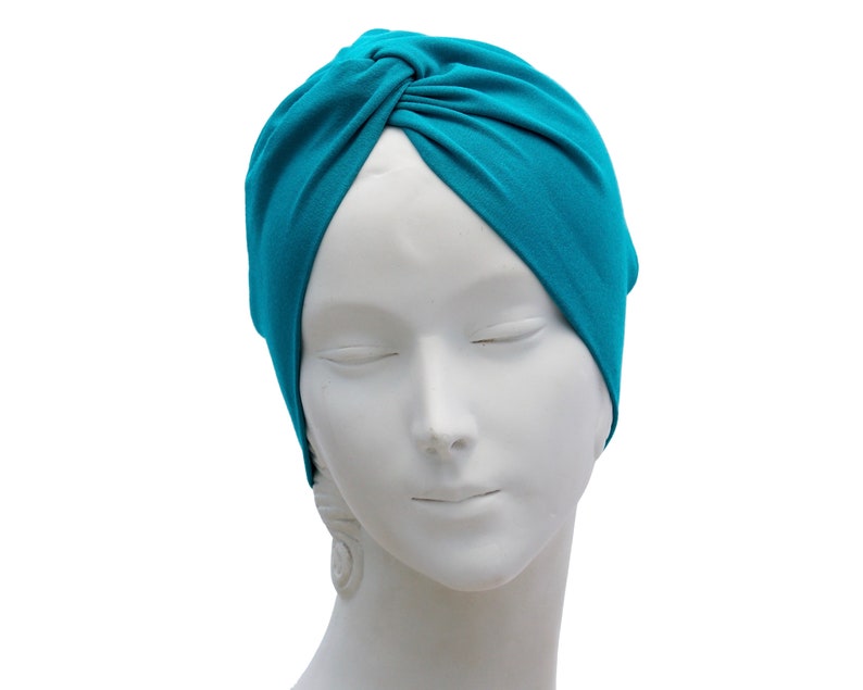 May include: A teal-colored turban-style head covering. The fabric is gathered and knotted at the top, creating a stylish and comfortable accessory. The head covering is displayed on a white mannequin head.