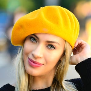 May include: A bright yellow beret made of felt. The beret is worn on the head of a person with blonde hair.