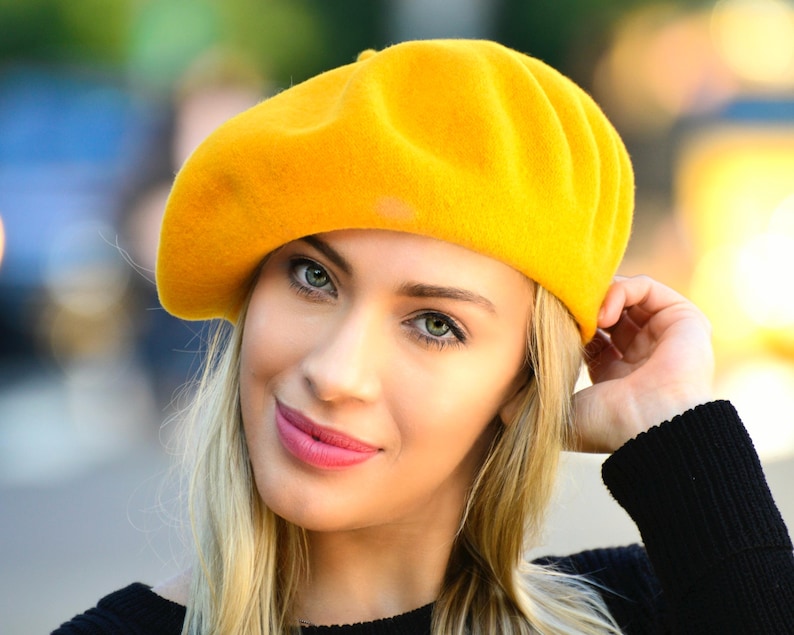 May include: A bright yellow beret made of felt. The beret is worn on the head of a person with blonde hair.