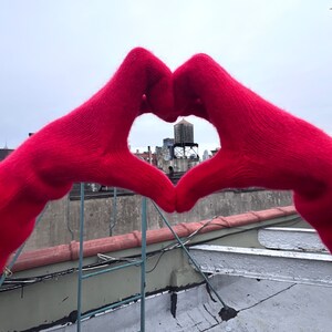 May include: A pair of red knitted gloves forming a heart shape with a city skyline visible through the opening.