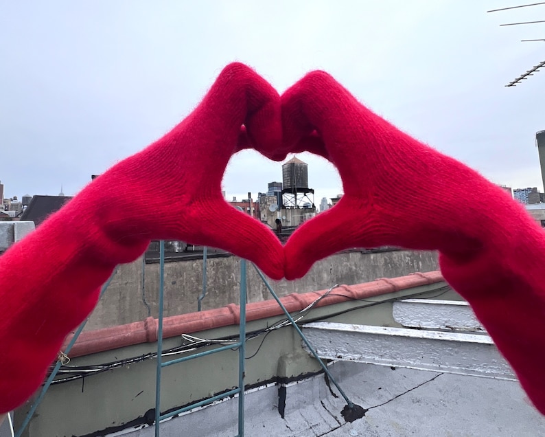 May include: A pair of red knitted gloves forming a heart shape with a city skyline visible through the opening.