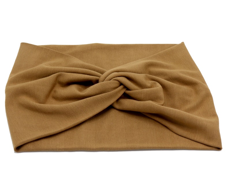 May include: A tan-colored, knotted headband made of soft fabric. The headband is a solid color and has a twisted knot detail at the center. The fabric appears to be a knit or jersey material, suitable for casual wear.