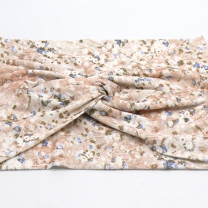 May include: A beige and brown floral patterned headband with a twisted knot design. The fabric features small blue and green floral accents. This accessory is designed to be worn around the head.