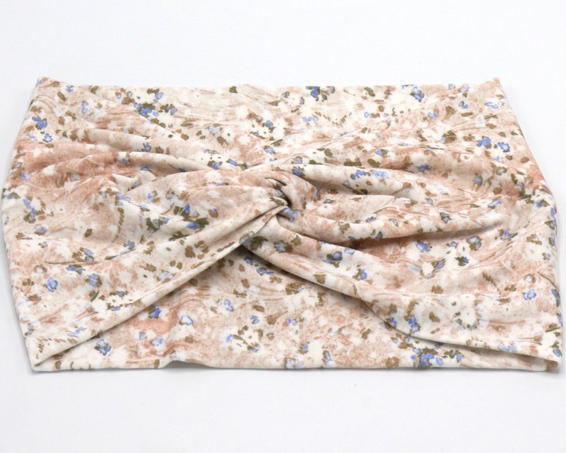 May include: A beige and brown floral patterned headband with a twisted knot design. The fabric features small blue and green floral accents. This accessory is designed to be worn around the head.