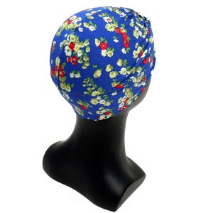 May include: A blue turban with a floral pattern of red, white, and green flowers. The head covering is displayed on a black mannequin head. The fabric appears to be soft and lightweight, suitable for various occasions.