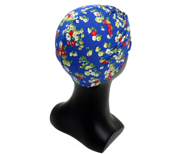 May include: A blue turban with a floral pattern of red, white, and green flowers. The head covering is displayed on a black mannequin head. The fabric appears to be soft and lightweight, suitable for various occasions.