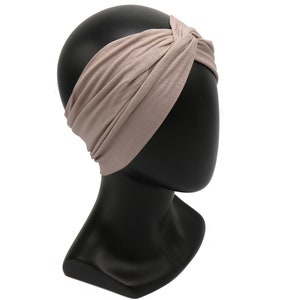 May include: A taupe-colored headband with a twisted knot design. The wide headband is made of a soft, stretchy fabric and is displayed on a black mannequin head. This accessory is suitable for various hairstyles and adds a touch of style.