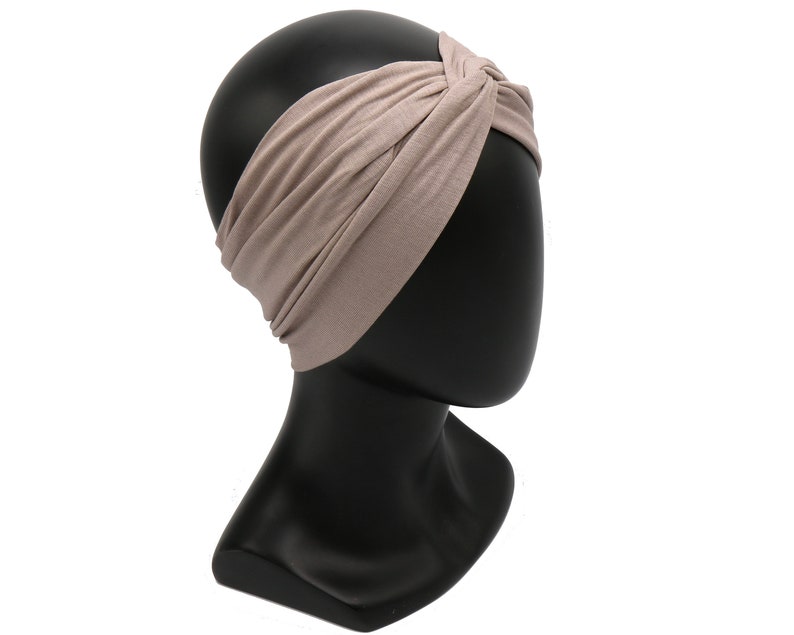 May include: A taupe-colored headband with a twisted knot design. The wide headband is made of a soft, stretchy fabric and is displayed on a black mannequin head. This accessory is suitable for various hairstyles and adds a touch of style.