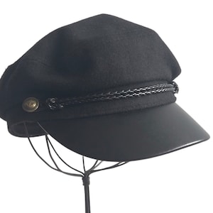 May include: A black wool cap with a black leather brim and a braided black band around the crown. The cap has a gold button on the front.
