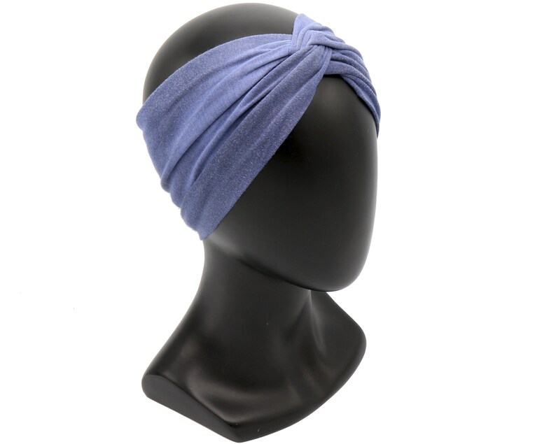 May include: A periwinkle blue headband with a twisted knot design. The fabric has a subtle, textured appearance. The headband is displayed on a black mannequin head, showcasing its shape and style. This accessory is designed for hair styling.