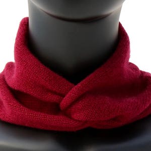 May include: A burgundy knitted neck warmer or scarf. The scarf is folded and worn around the neck.
