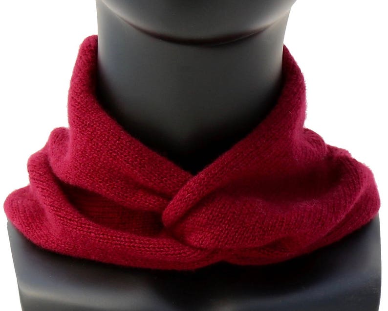 May include: A burgundy knitted neck warmer or scarf. The scarf is folded and worn around the neck.