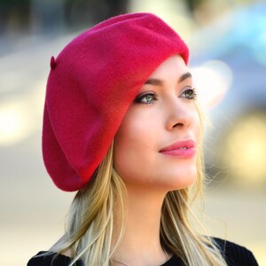 May include: A woman wearing a bright red beret. The beret is made of felt and has a simple design.