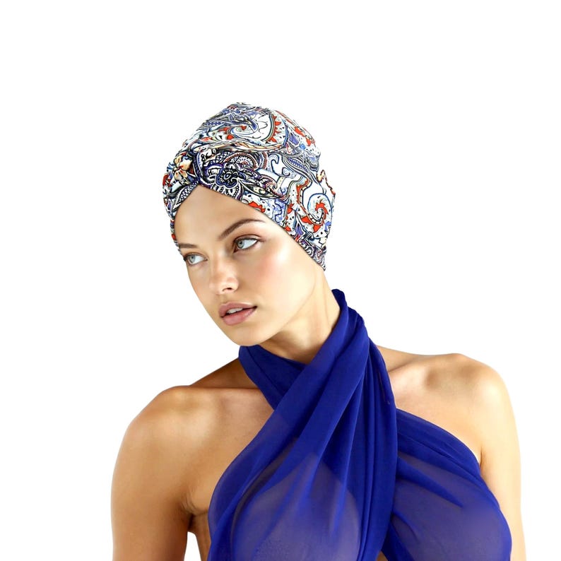 May include: A patterned turban with a paisley design in shades of blue, red, and white. The turban is worn with a draped blue fabric. The image is set against a white background.