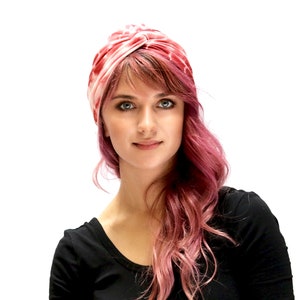 May include: A pink and white turban-style head covering. The head wrap is made of a soft, silky material. The woman in the image is wearing a black top and has pink hair.