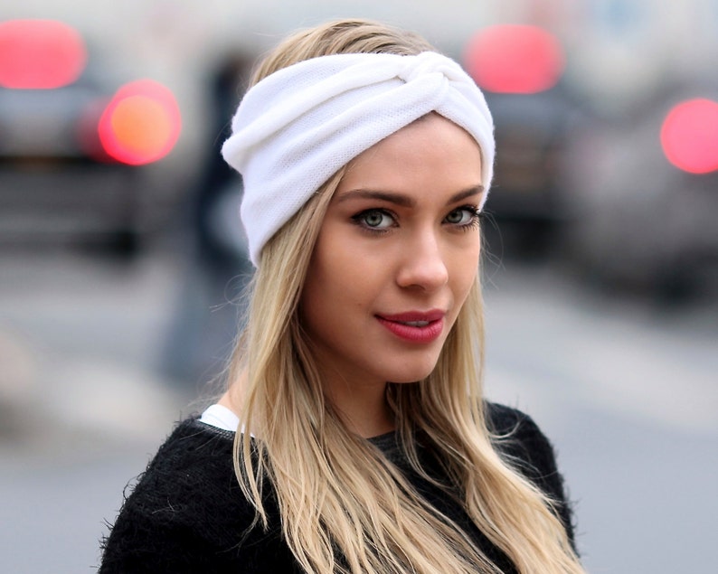 May include: A woman with long blonde hair is wearing a white turban headband. The headband is made of a soft, stretchy fabric and has a knotted design.