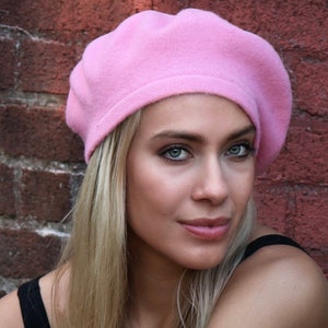 May include: A woman wearing a pink beret. She has long blonde hair and is looking at the camera.
