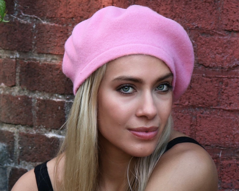 May include: A woman wearing a pink beret. She has long blonde hair and is looking at the camera.