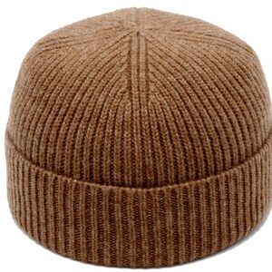 May include: A brown, ribbed knit beanie hat. The hat is a solid color and has a folded brim. The knit pattern is vertical, creating a textured appearance. The hat is a classic style, suitable for cold weather.