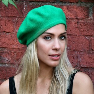 May include: A woman wearing a bright green beret. She has long blonde hair and is wearing a black tank top.
