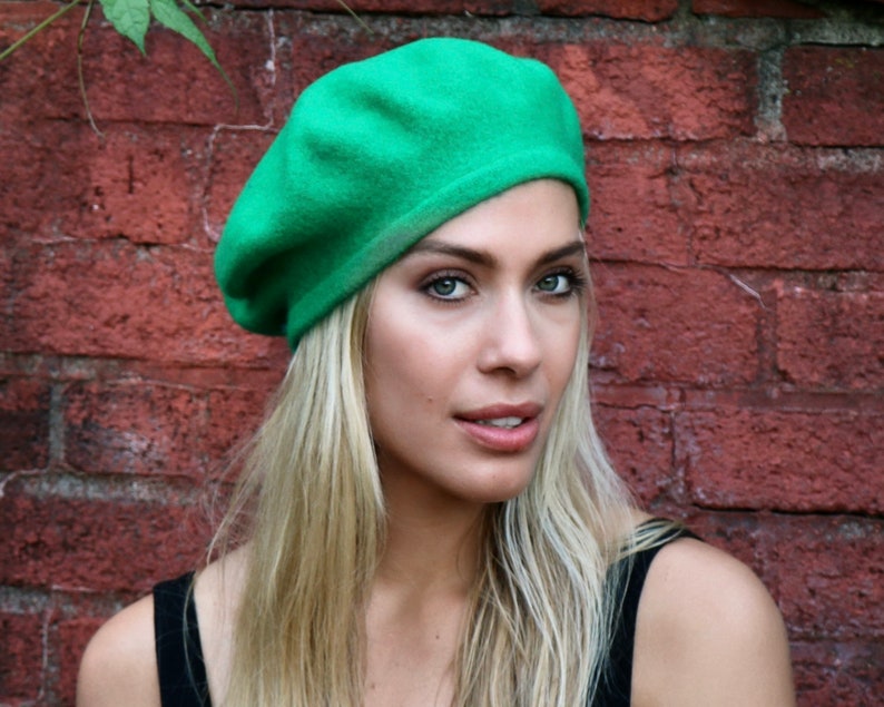 May include: A woman wearing a bright green beret. She has long blonde hair and is wearing a black tank top.