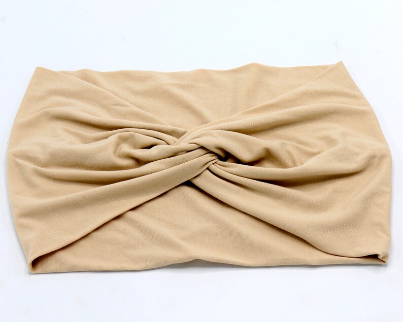 May include: A tan-colored, knotted headband made of soft fabric. The headband is folded and twisted at the center, creating a stylish and comfortable accessory. This hair accessory is suitable for various hairstyles.