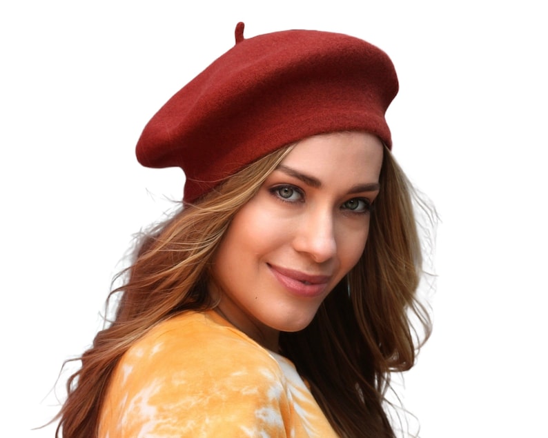 May include: A woman wearing a red beret and a yellow and white tie-dye shirt.