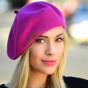 May include: A woman wearing a bright pink beret. The beret is made of felt and has a classic style.