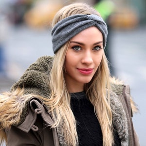 May include: A woman with long blonde hair wearing a gray knitted headband, a brown jacket with a fur trim, and a black sweater.