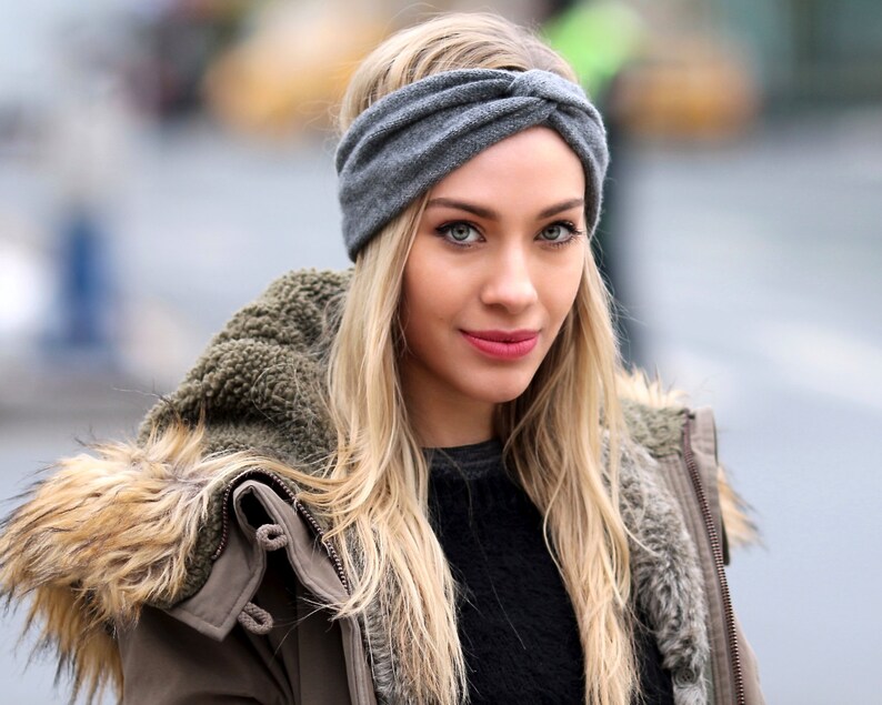 May include: A woman with long blonde hair wearing a gray knitted headband, a brown jacket with a fur trim, and a black sweater.