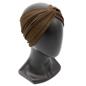May include: A brown knotted headband displayed on a black mannequin head. The headband is made of a soft, textured fabric and features a twisted knot detail at the top. The head covering is designed to keep hair out of the face.