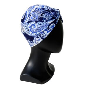 May include: A blue and white paisley patterned turban. The head covering is displayed on a black mannequin head. The fabric features a dark blue background with swirling paisley designs in shades of blue and white.