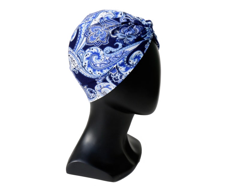 May include: A blue and white paisley patterned turban. The head covering is displayed on a black mannequin head. The fabric features a dark blue background with swirling paisley designs in shades of blue and white.