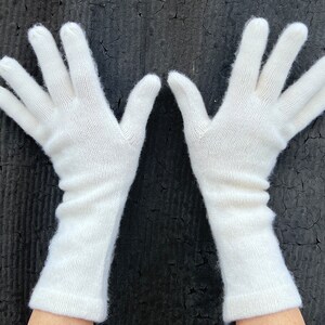 May include: A pair of long white knitted gloves. The gloves are made of a soft, fine knit material.
