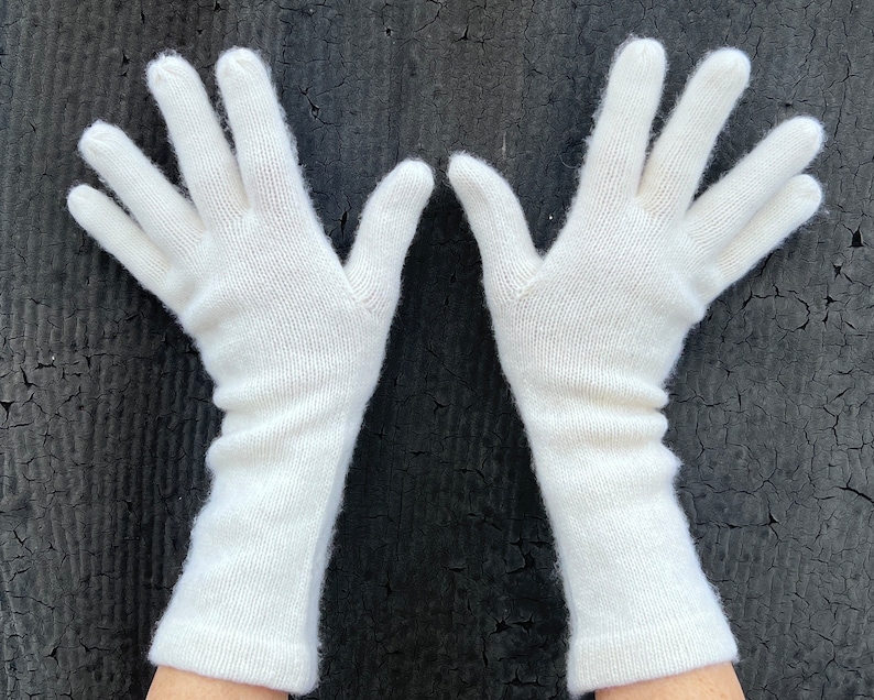 May include: A pair of long white knitted gloves. The gloves are made of a soft, fine knit material.