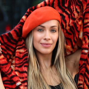 May include: A woman wearing a bright orange beret and a tiger print scarf. The scarf is draped over her shoulders and the beret is tilted slightly to the side.
