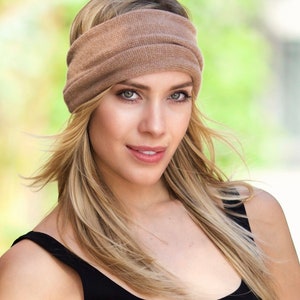 May include: A woman with long blonde hair is wearing a brown knitted headband. The headband is wide and covers her forehead. She is wearing a black tank top.