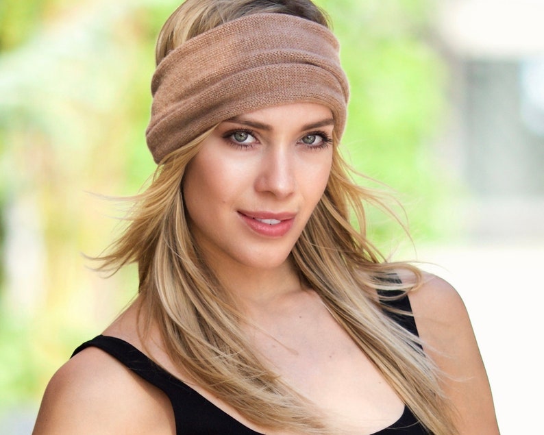 May include: A woman with long blonde hair is wearing a brown knitted headband. The headband is wide and covers her forehead. She is wearing a black tank top.