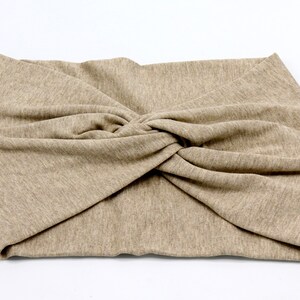 May include: A beige-colored headband with a twisted knot design. The fabric appears to be a soft knit material. The headband is designed to be worn around the head, likely for fashion or to keep hair out of the face.