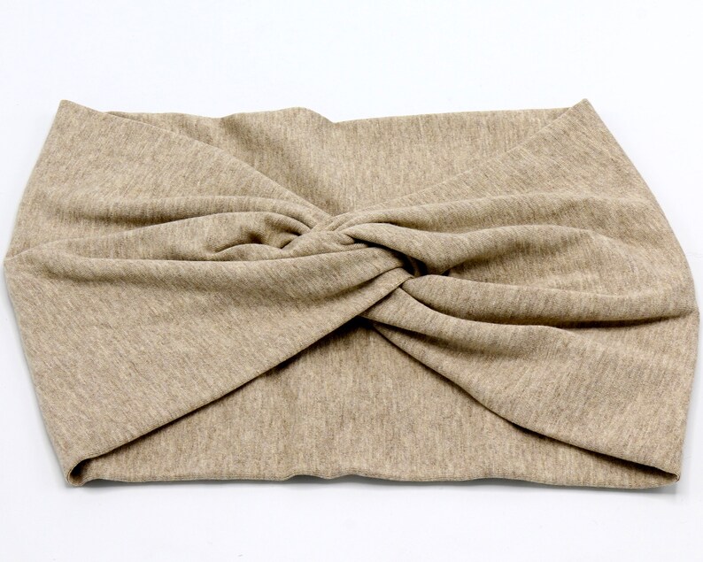 May include: A beige-colored headband with a twisted knot design. The fabric appears to be a soft knit material. The headband is designed to be worn around the head, likely for fashion or to keep hair out of the face.