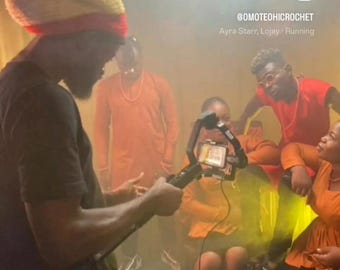 Puede incluir: Un grupo de personas, algunas vestidas de naranja, se reúnen en un espacio con poca luz. Una persona lleva un sombrero con rayas verdes, amarillas y rojas. Se ve el nombre de usuario de Instagram @OMOTEOHICROCHET y el texto "Ayra Starr, Lojay - Running".
