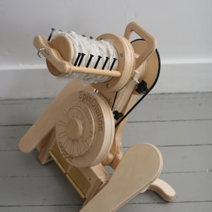 May include: A wooden spinning wheel with a white yarn bobbin, a black belt, and the text "SpinOlution" and "Support" on the wheel.